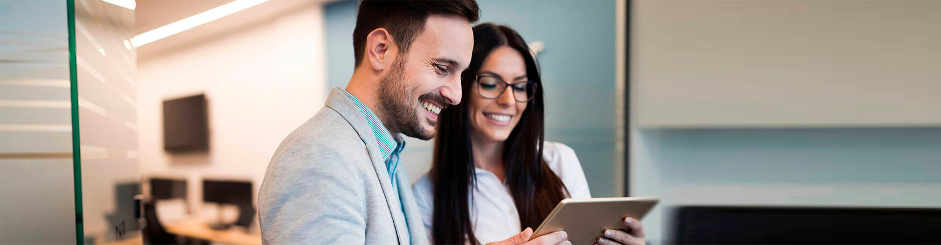 Cash Pooling - Hombre de traje sonriendo junto a una mujer de gafas sonriendo en oficina Cash Pooling - Hombre de traje sonriendo junto a una mujer de gafas sonriendo en oficina