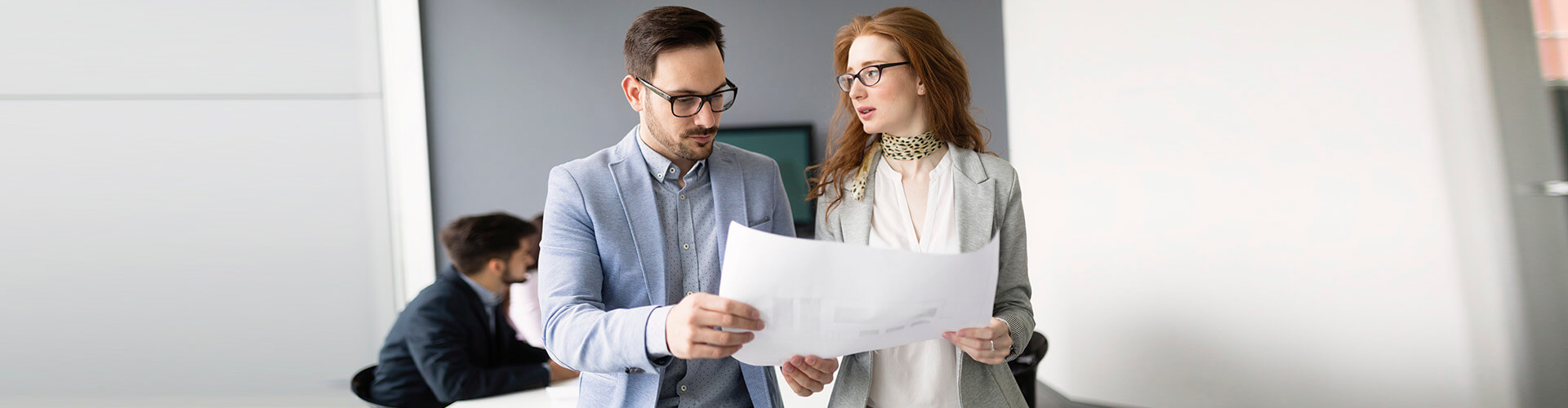 Seguro de Credito - Reunion de negocios entre una mujer con traje gris y un hombre de traje azul mientras estan leyendo unos papeles en una sala de reuniones Seguro de Credito - Reunion de negocios entre una mujer con traje gris y un hombre de traje azul mientras estan leyendo unos papeles en una sala de reuniones