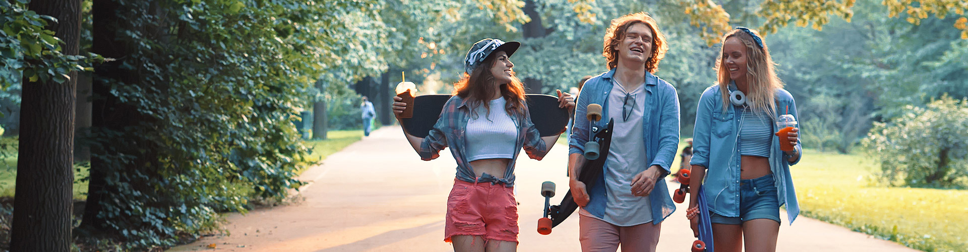 Programa Joven In - Grupo de jovenes vestidos con ropa moderna con patinetes, sonriendo junto a un parque rodeado de arboles